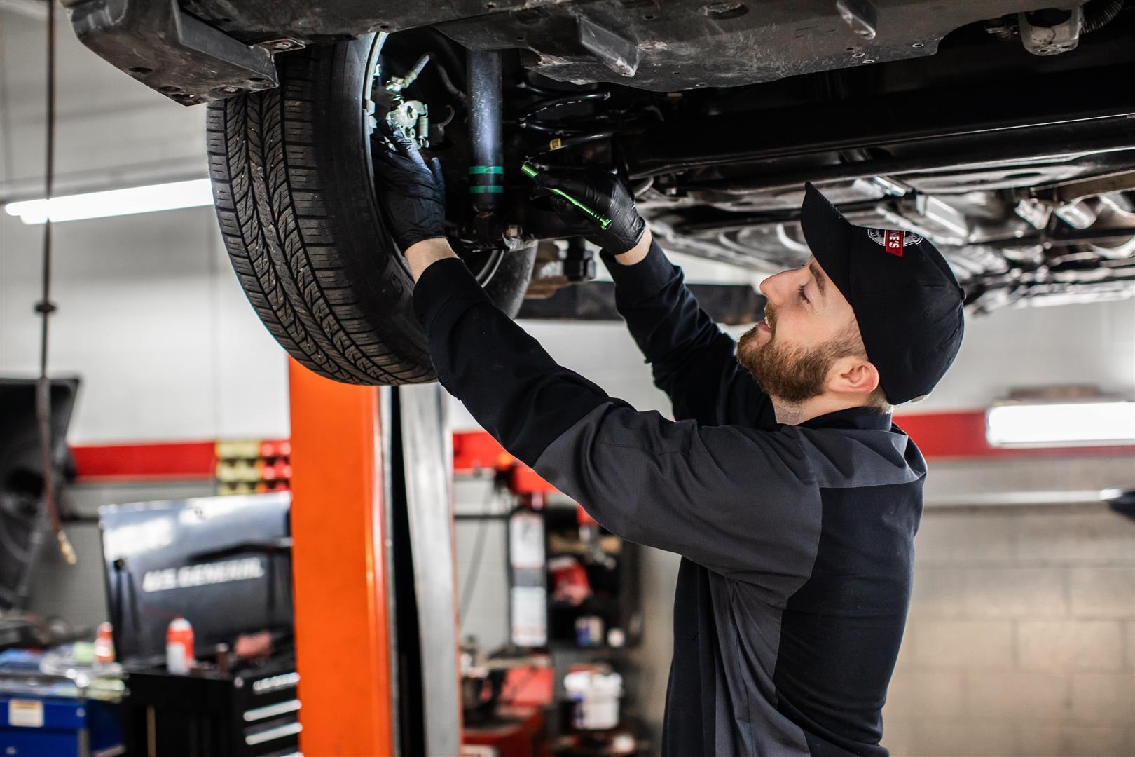 Auto repair technician inspecting a wheel and brakes of a lifted car
