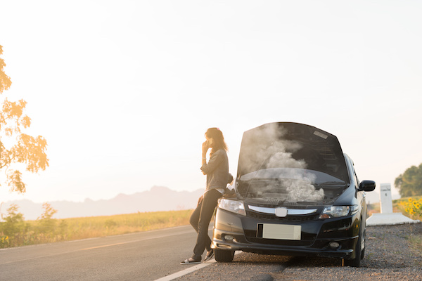 Woman beside her smoking car, calling for help on her phone