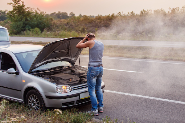 A broken car at the side of the road and its owner, hands on his head