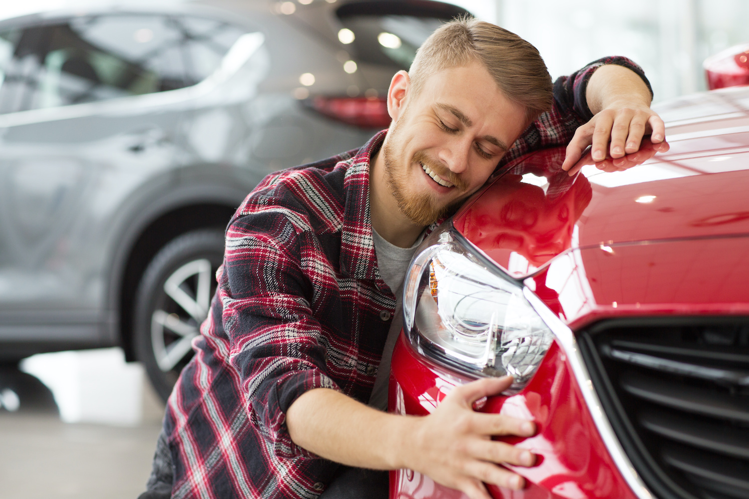 A happy car owner embracing his newly-repaired red sedan