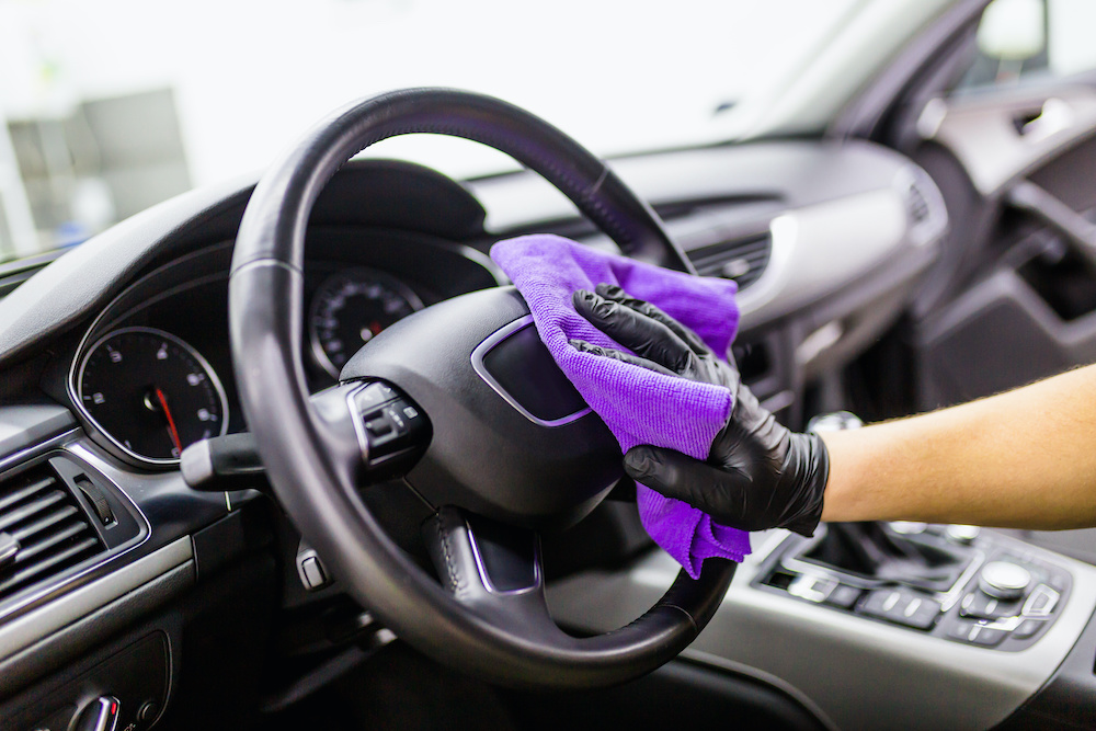 Gloved hands wiping the dashboard clean with microfiber cloth