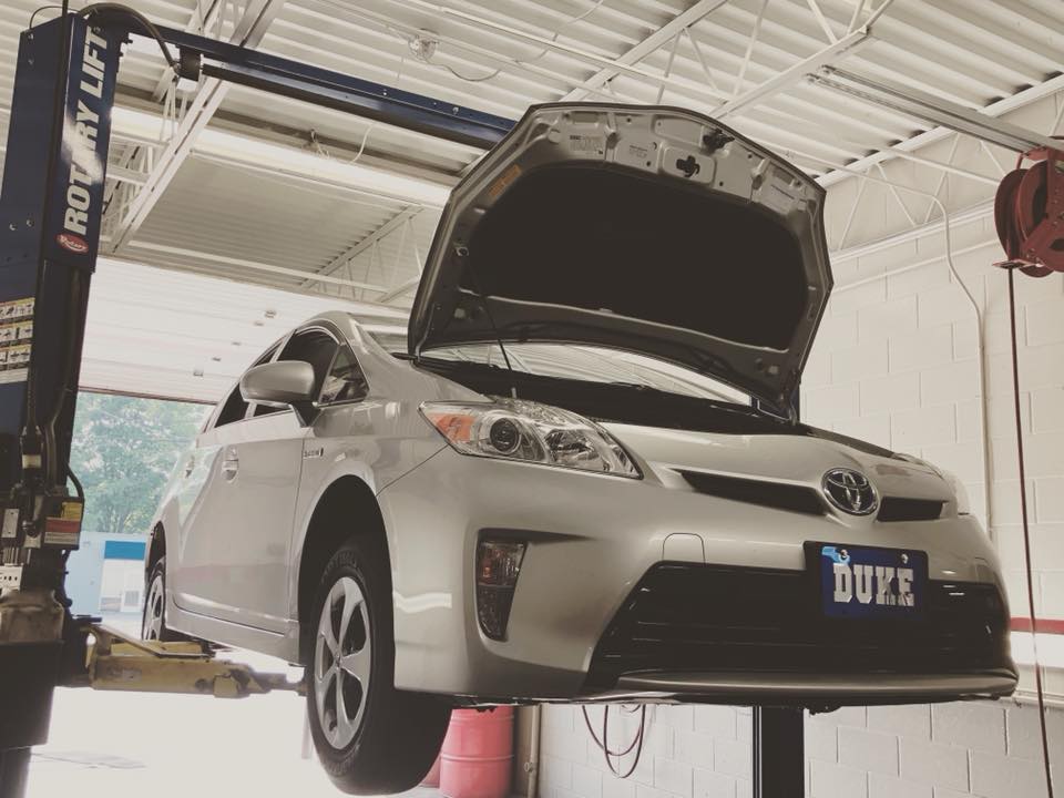 A white Toyota sedan on a lift, under repair with an open hood