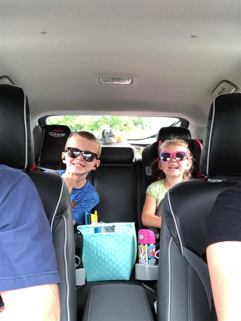 Young siblings broadly grinning at the backseat of their family car